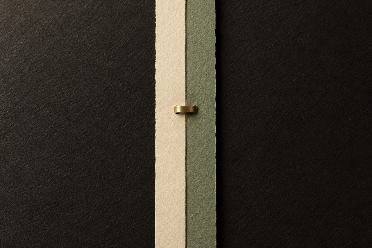 Two strips of warm cream paper overlapping on a black surface, with a deep-green thread along one edge